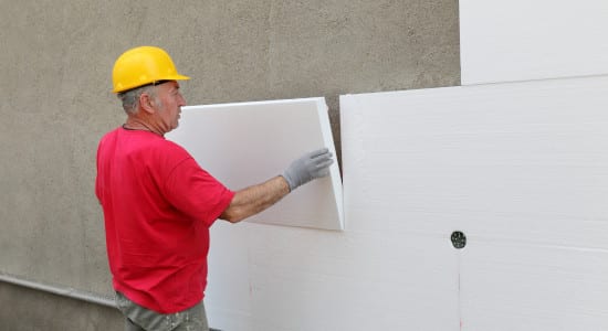 Artisan pose des plaques de polystyrènes pour une isolation de mur par l'extérieur