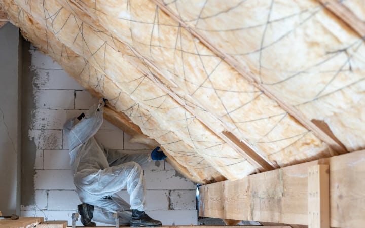 Artisan posant un isolant en laine de roche sous la face intérieur de la toiture sous les combles aménageables